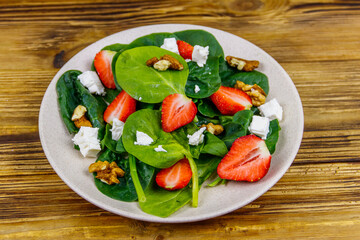 Fresh healthy salad with strawberry, spinach, walnuts and feta cheese on wooden table