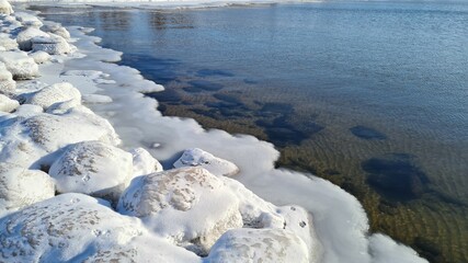 In the winter, the Baltic Sea and ice covered the frozen rocks at dawn. Baltic Sea - winter beach with frozen stones. The picturesque landscape of the Baltic Sea in the polar winter