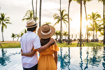 Young couple traveler relaxing and enjoying the sunset by a tropical resort pool while traveling...