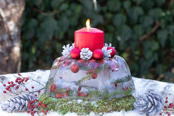 Eis-Laterne mit roter Kerze, Zapfen und Christbaumkugeln als Weihnachtsdekoration
