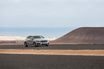 Grey car driving empty paved road in desert volcanic landscape