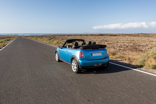 Blue cabrio car driving empty paved road in desert volcanic landscape