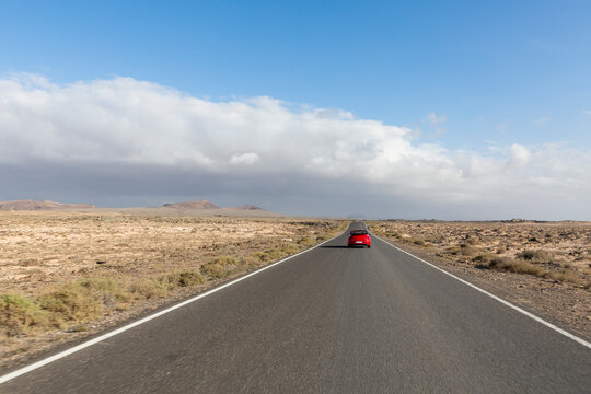 Red cabrio car driving empty paved road in desert volcanic landscape