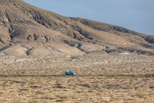 Red cabrio car driving empty paved road in desert volcanic landscape