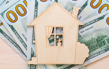 Model of a wooden house on a wooden background with dollars, top view . The theme of the construction, buying a new home.