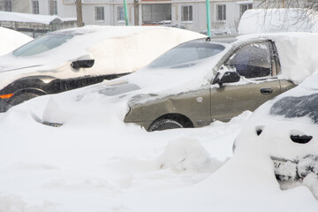 Parked cars covered in snow, selective focus. Snowfall in the city, falling snowflakes. Concept: traffic collapse, replacement of summer tires with winter tires, increased precipitation and snow level