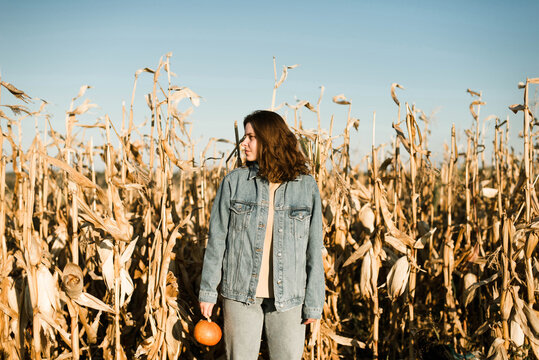Portrait of woman holding pumpkin in the middle of a corn field