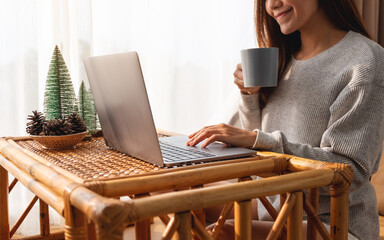 Closeup image of a beautiful young asian woman using and working on laptop computer while drinking coffee at home