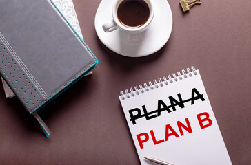 On a brown background, diaries, a white cup of coffee and a notebook with inscription PLAN B