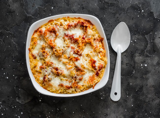 Baked orzo pasta with tomato sauce and mozzarella in a baking dish on a dark background, top view