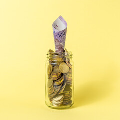 Golden coins in a glass jar. Savings money concept on light yellow background.