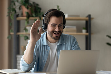 Distance is not a problem. Positive young guy in headset practice foreign language communicate online with native speaker using laptop. Millennial man remote student wave hand greet prof by video call