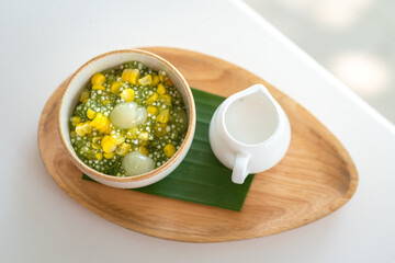 Sago or Saku topping with corn, longan fruits and coconut milk, served in white bowl on the wooden plate. This is one of famous tradition Thai dessert food. Sweet food close-up photo.
