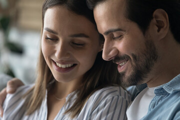 Close up shot of affectionate loving husband sit close hug shoulders of beloved young wife. Smiling faces of romantic millennial couple embracing dreaming talking sharing feelings emotions memories