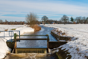 Small dam in river in winter landscape with trees