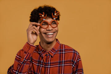 Photo of cute African male farmer wears Christmas glasses and smiles. Man wears plaid shirt, isolated brown color background