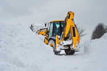 Yellow tractor excavator with large bucket clears snowy road from snow