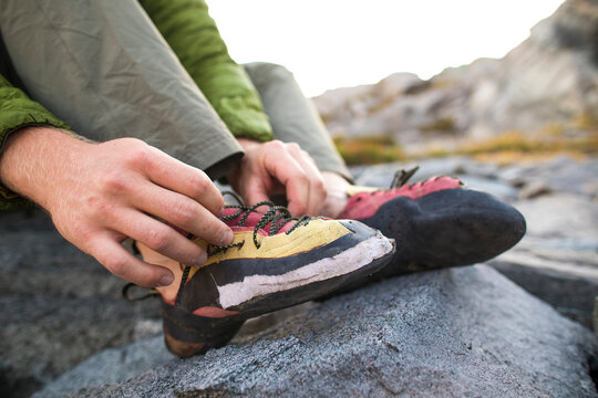 Rock climber laces up his worn climbing shoes