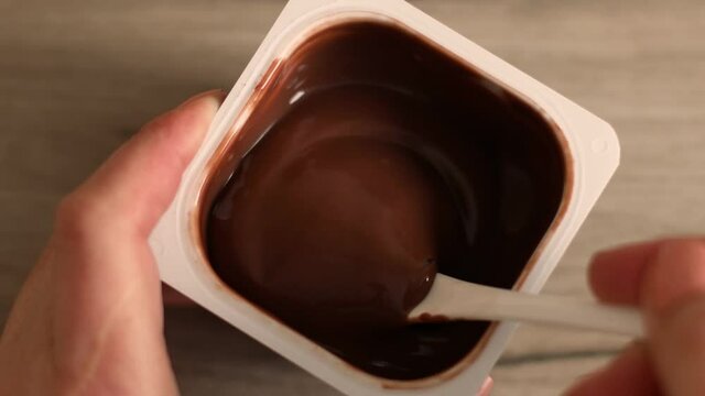 Close up of man hands take a delicious chocolate mousse or pudding with spoon in a plastic jar