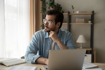 Pensive young guy employee sit at workplace look aside of pc screen think on problem of research...