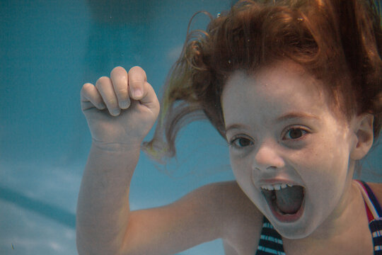 five year old girl underwater smiling in pool
