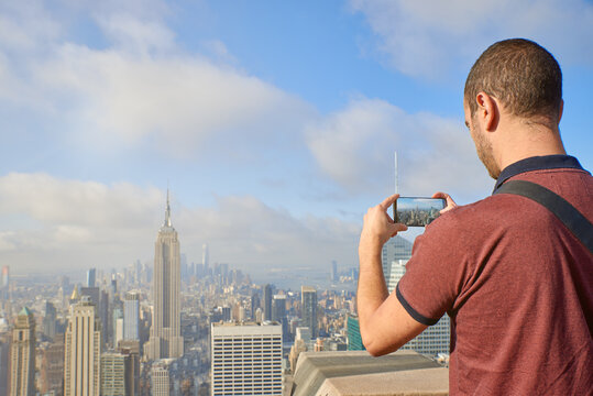 USA, New York City, Tourist taking picture with smart phone with view of Manhattan skyline and East River