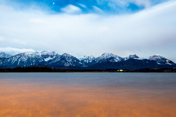 Long exposure panorama of the alps at night with the hopfensee in the foreground