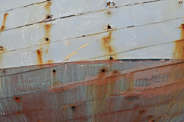 Cracked paint and rust on detail of boat hull showing planks. white and light blue.