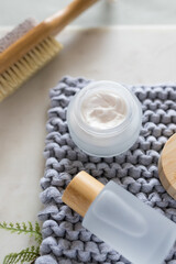 Cosmetic set for body care on a knitted cloth over a white marble board next to a blurred double face brush.