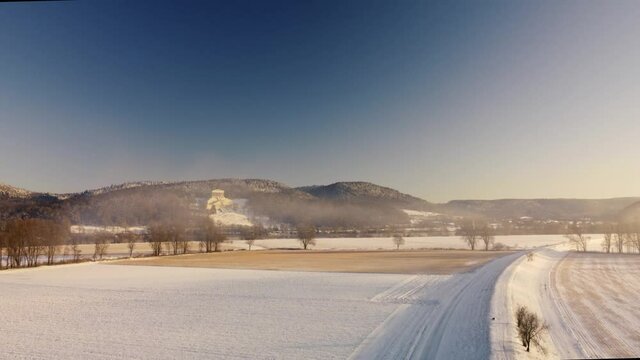 Drone flying towards historic landmark Walhalla in Donaustauf near Regensburg in Bavaria on danube river in beautiful winter landscape with snow on sunny day