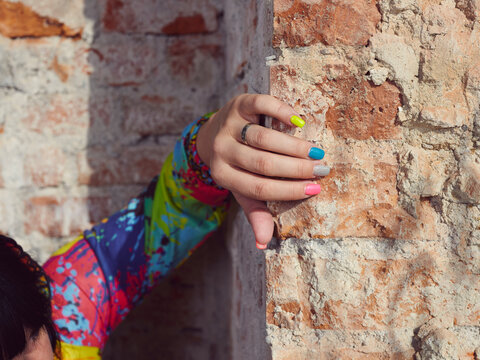 Close up of female hands with coloured nails on brick wall