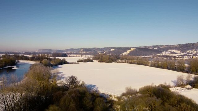 Drone rising over beautiful bavarian winter landscape with snow and famous landmark Walhalla over the Danube river in background on clear sunny day