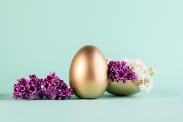 Easter egg painted in gold color decorated with purple lilac floewrs. Happy Easter minimalistic background.
