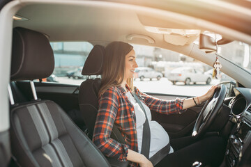 Pregnant happy woman driving with safety belt on in the car.