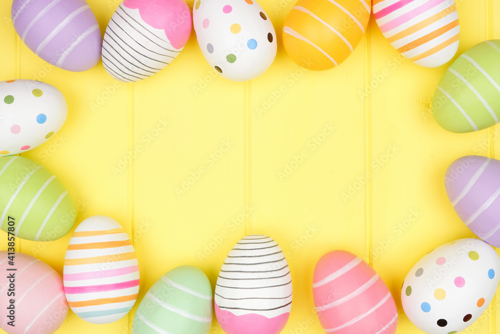 Poster colorful easter egg frame over a soft yellow wood background. top down view with copy space.