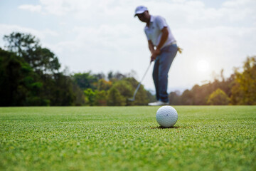 Blurred Golfer putting ball on the green golf, lens flare on sun set evening time. Golfer action to win after long putting golf ball in to the hole.