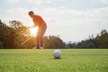 Golfer putting ball on the green golf, lens flare on sun set evening time. Golfer action to win after long putting golf ball in to the hole.