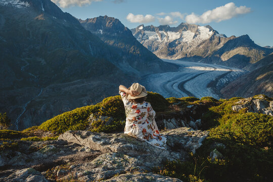 A woman in a flowered dress and straw hat sits at Aletch Glacier