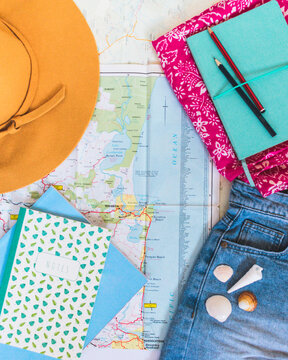 beach hat towel demin short shells pencil and notebook laid on map
