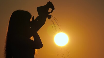 The girl plays pours water in the sun. A woman pours water on the sun from a watering can. Man grows sun. Gardener, farmer. Sunrise. The concept of life, peace, kindness. Beautiful sunset.