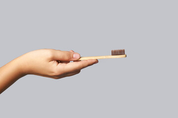 Hand holding toothbrush. Bamboo eco brush. Dental sustainable concept. Layout. Morning home routine. Grey background. Medicine cosmetics. Mouth hygiene treatment. Personal cleaning. Copyspace