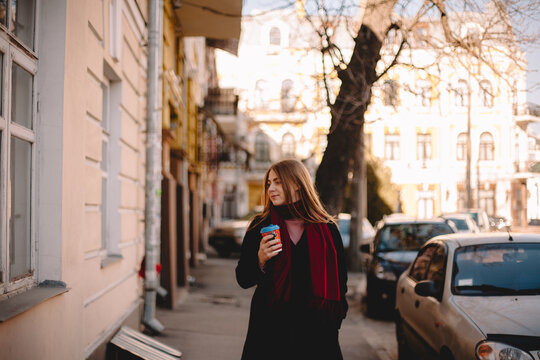 Portrait of young woman with coffee cup walking on sidewalk