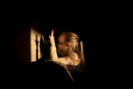 Little girl with long hair and glasses makes shadow puppets on wall