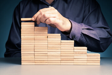 Man add wooden block piece by piece to build a high stairs step, long term achievement, investment