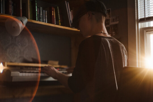 Teenage boy plays keyboard in bedroom during sunset