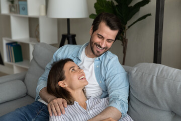 Serene young wife lie on sofa rest feel love safe comfort in caring husband arms hold pleasant talk...