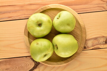 Several juicy green apples on a round
  wooden tray on a wooden table, close-up, top view.