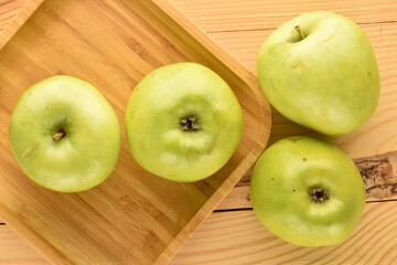 Several ripe green apples in a bamboo dish on a wooden table, close-up, top view.