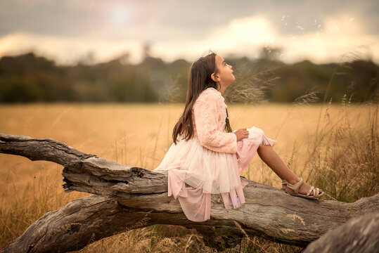 little girl sitting on tree branch looking up at wind blowing seeds