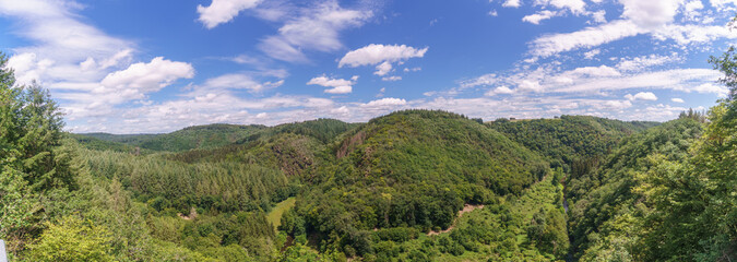 panorama of beautiful Eifel landscape of Lieser valley with forest over cloudy blue sky near...